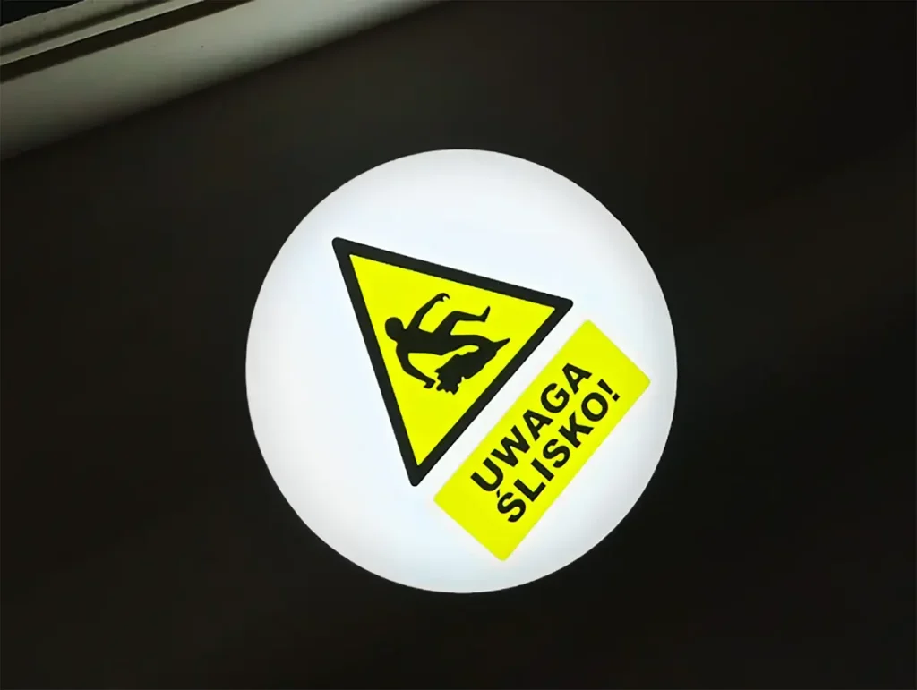 Znak ostrzegawczy UWAGA SLISKO wyswietlony projektorem GOBO na posadzce hali
